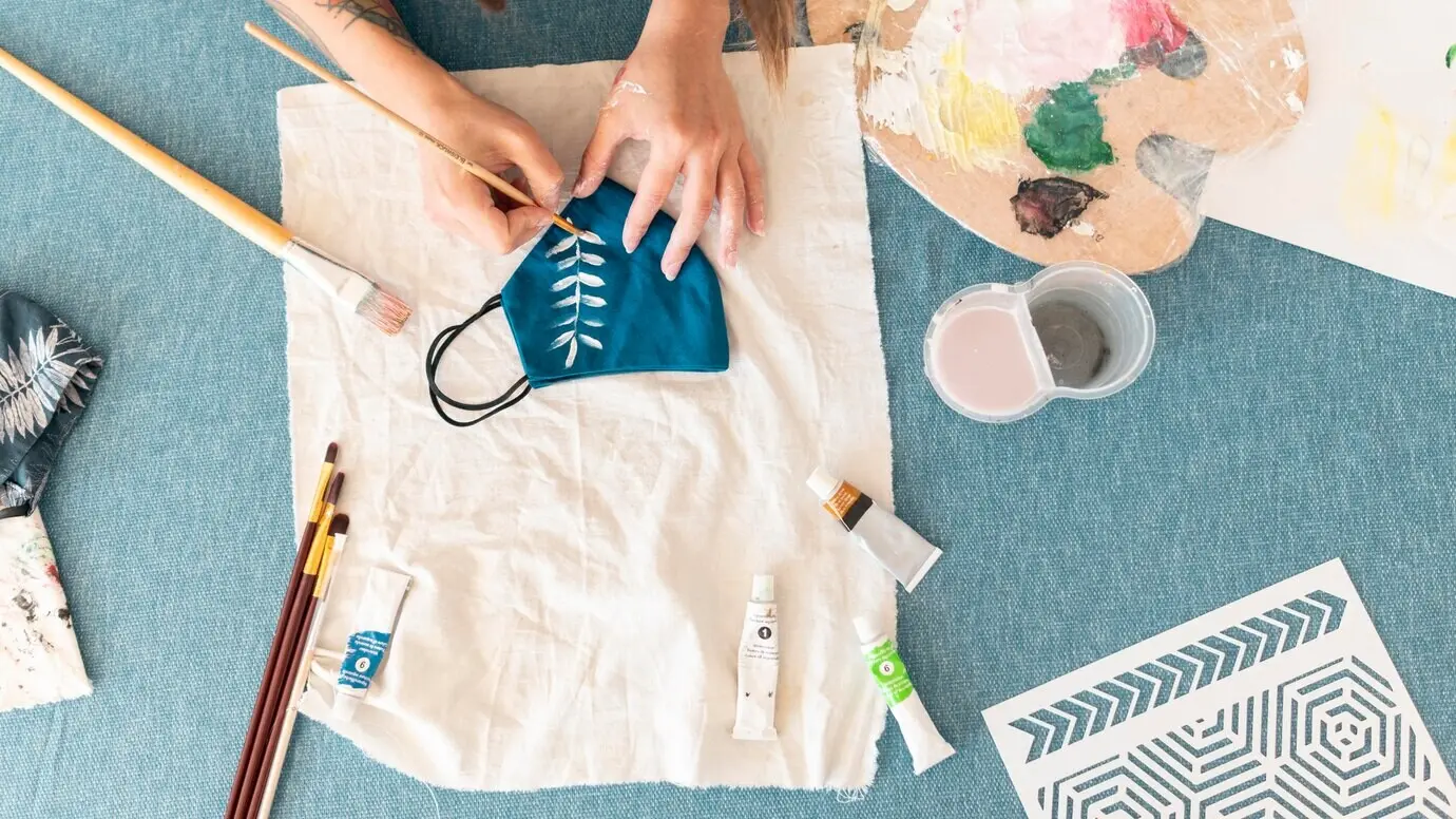 Hände bemalen eine Maske in Nahaufnahme aus der Draufsicht.